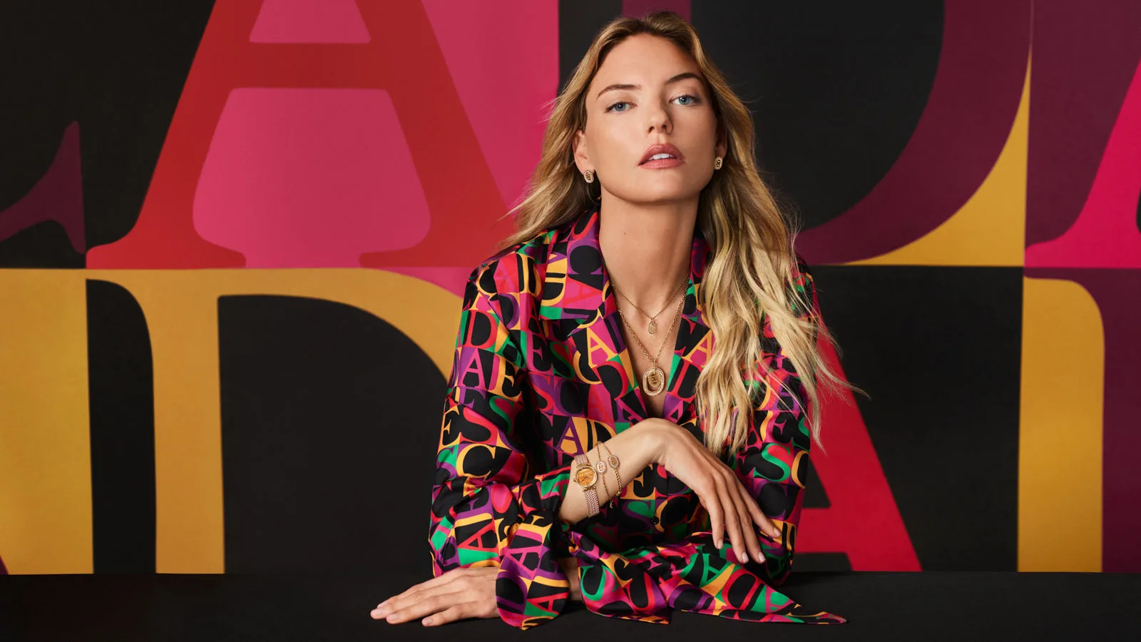 Campaña de ESCADA primavera/verano 2026: modelo con blusa de estampado de letras y joyas doradas