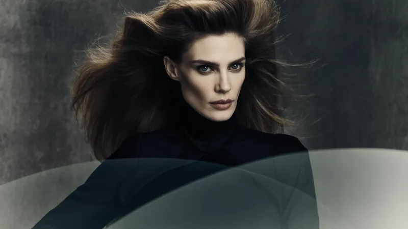 Retrato de una mujer con melena castaña al viento y jersey negro de cuello alto sobre fondo gris